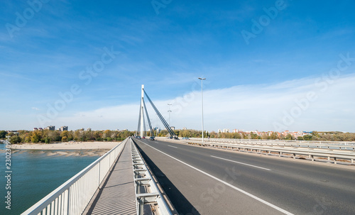 Liberty bridge over the Danube river with beach and building of Novi Sad city in Serbia with cars driving over and blue sky above