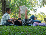 Cute two asian student boy reading book in the nature park with sunlight  background, people, learning, relax, education and Natural classroom concept..