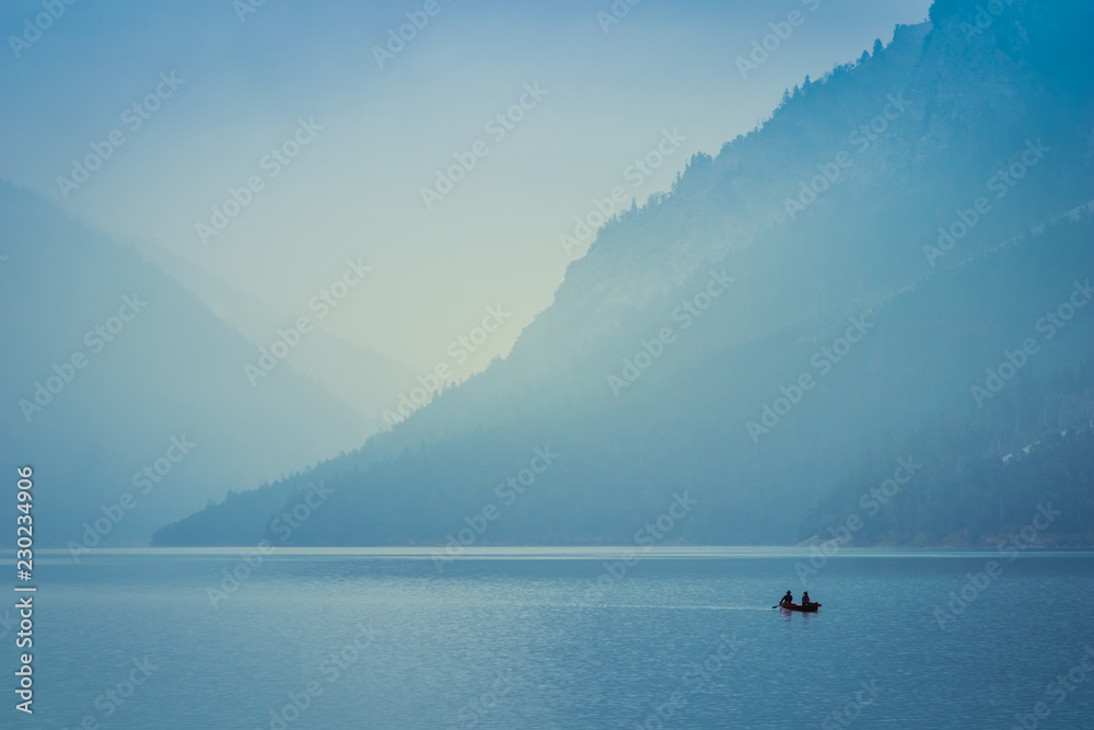 Two people rowing a small boat on lake Plansee in the European Alps, in Austria at early morning sunrise