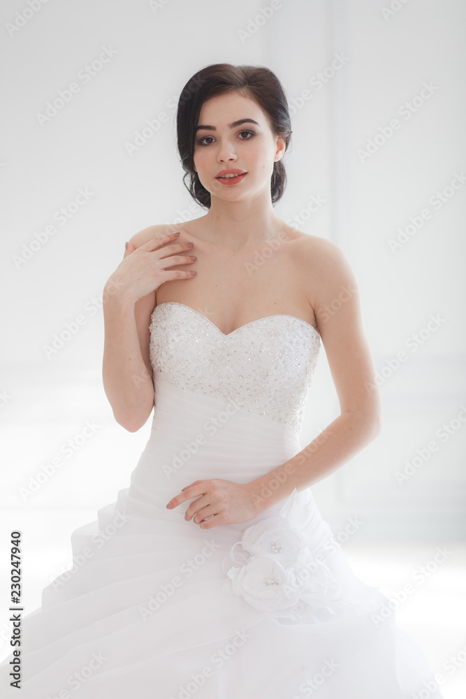 The beautiful young woman posing in a wedding dress over grey background studio room. Half-lenght portrait The beautiful young woman posing in a wedding dress over grey background studio room. Half-lenght portrait