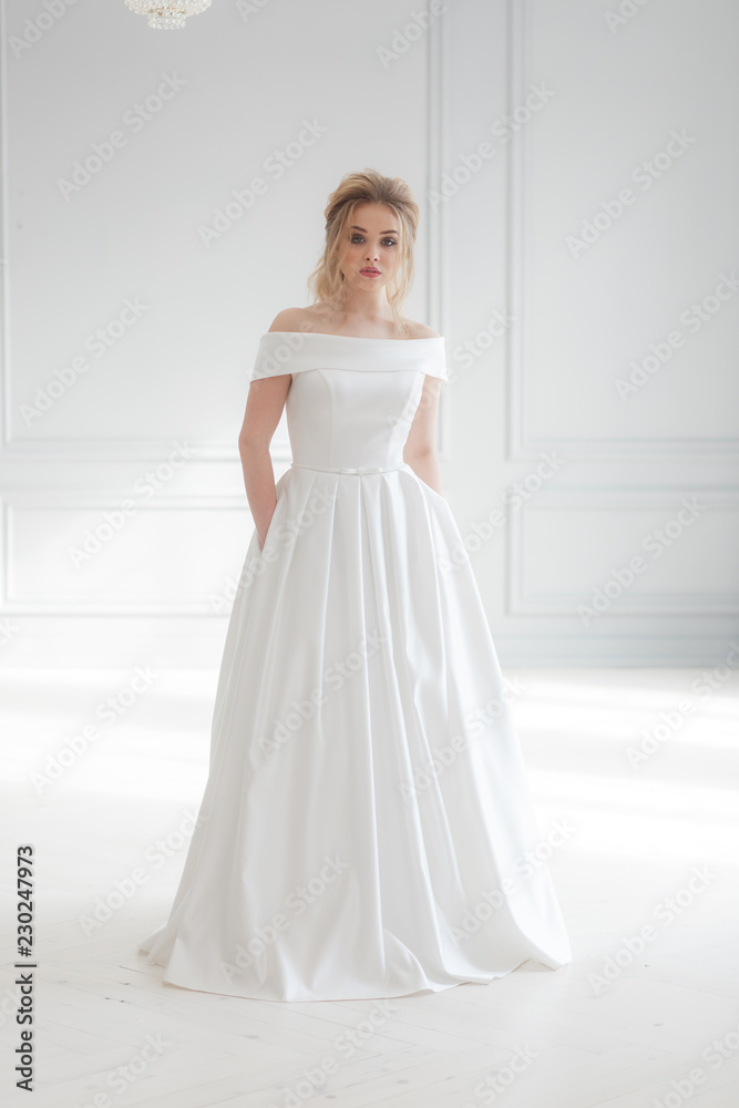 Young beautiful bride wearing white wedding dress in light classic studio interior. Vertical full-lenght portrait Young beautiful bride wearing white wedding dress in light classic studio interior. Vertical full-lenght portrait