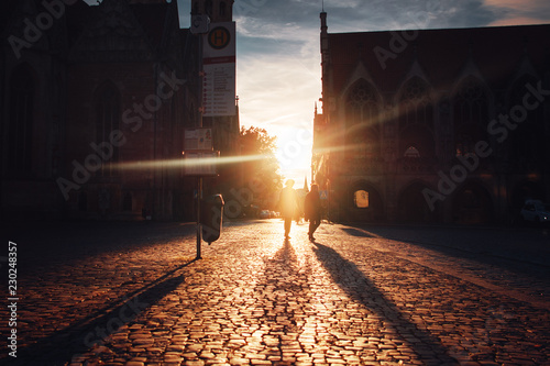 Historic cobblestone street view with a church and old town city hall at colorful sunset light and persons crossing the street and long shadows. Altstadtmarkt, Braunschweig in Germany photo