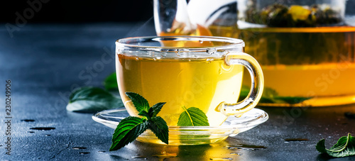 Hot chinese green tea with mint, with splash pouring from the kettle into the cup, steam rises, dark background, selective focus