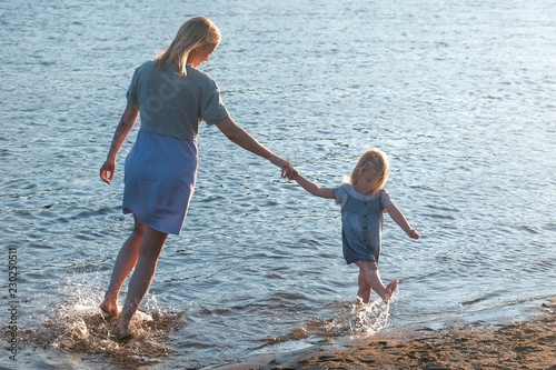 Mom and girl playing on the beach of the river at sunset and swim.