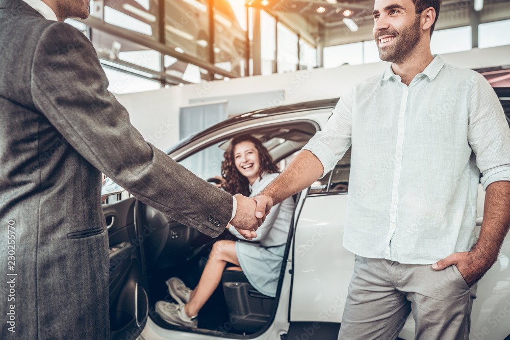 Obraz premium close up view of handshake of salesmen with the man in the showroom on the background of a woman in a new car