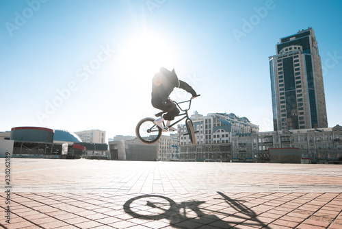Street portrait of a bmx rider in a jump on the street in the background of the city landscape and the sun. Bmx concept. Street freestyle on bmx