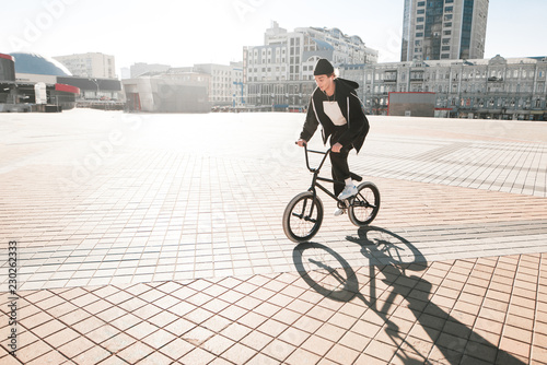 BMX cyclists ride a bike on the square on a sunny day. Young rider bmx bicycle walks through the city. BMX concept © bodnarphoto