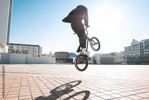 Bmx rider makes a trick in the jump on the street in the background of the city landscape and the sun. Bmx concept. Street freestyle on bmx