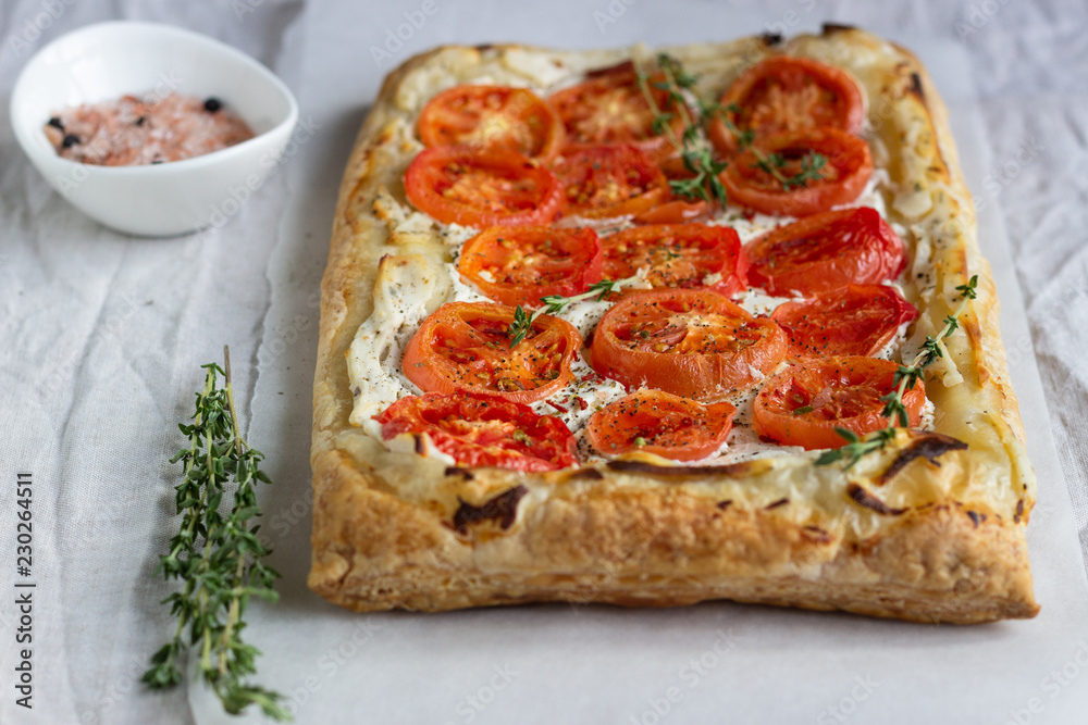 Deliciously simple tomato tart, puff pastry topped with cream cheese or ricotta and tomatoes on parchment paper. Summer tart. Top view. Copy space