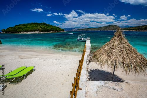 Spring daytime beautiful Ionian Sea with clear turquoise water  wooden pier and fine sand coast view from Ksamil beach  Albania. Deep blue sky with white clouds.