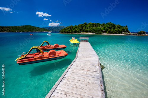 Spring daytime beautiful Ionian Sea with clear turquoise water, wooden pier and fine sand coast view from Ksamil beach, Albania. Deep blue sky with white clouds. photo