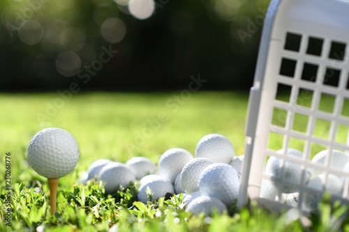 Golf ball on tee and golf balls in basket on green grass