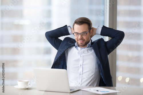 Photos Man sitting at table near laptop in office and feeling success or satisfaction