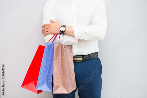 Closeup of buyer standing and holding shopping bags. Man keeping his arms crossed. Shopping concept. Isolated cropped view on grey background.