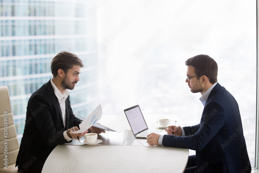 Two caucasian men sitting in front of each other at the table and discussing project results. Partners or manager and subordinate conduct performance evaluation appointment in office or meeting room Two caucasian men sitting in front of each other at the table and discussing project results. Partners or manager and subordinate conduct performance evaluation appointment in office or meeting room
