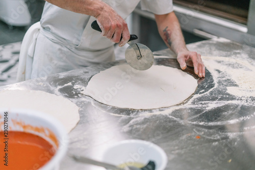 Cooking Italian national food with chef and ingredients for pizza. Dough in chef hand on a dark black background of wood. Baking bread, pizza, pasta. Recipe from chef cooks pizza.