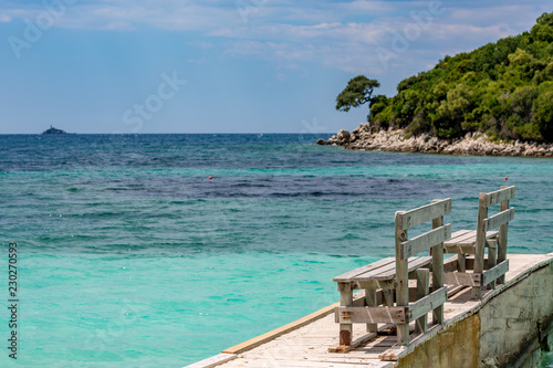 Spring daytime beautiful Ionian Sea with clear turquoise water, wooden pier and fine sand coast view from Ksamil beach, Albania. Deep blue sky with white clouds.