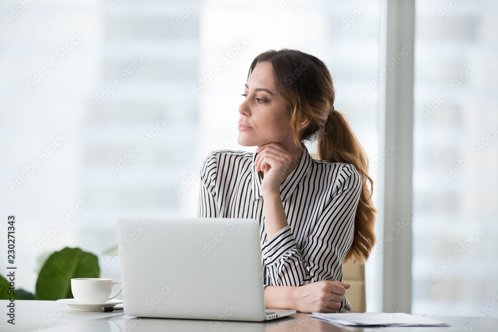 Focused pensive young woman looking in distance in window. Businesswoman at workplace behind laptop. challenging work, task, thinking about strategy, business projects. Business vision concept Focused pensive young woman looking in distance in window. Businesswoman at workplace behind laptop. challenging work, task, thinking about strategy, business projects. Business vision concept