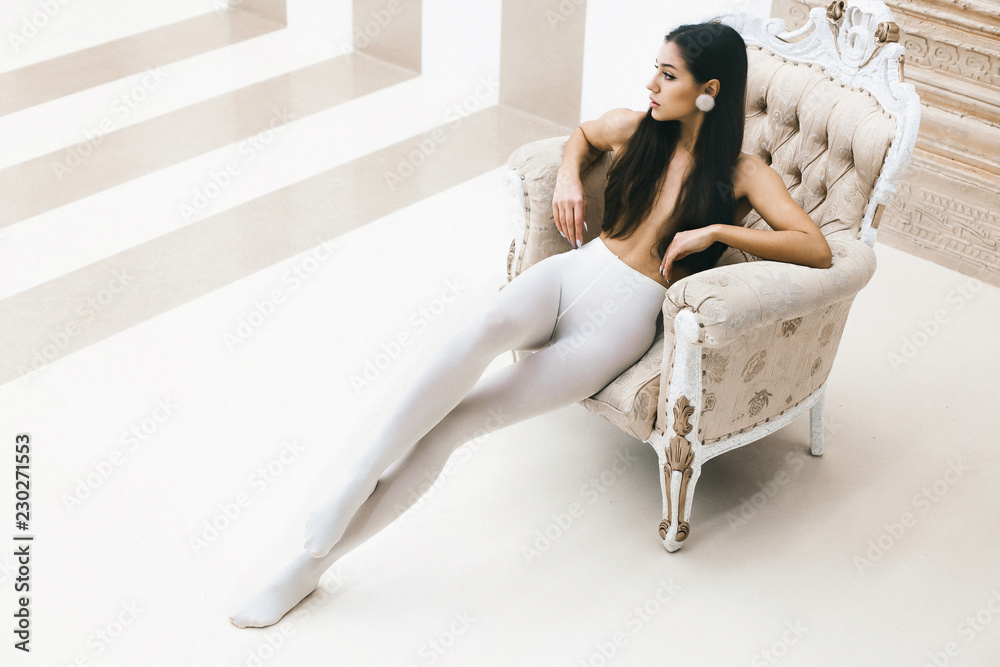 Young elegant girl in white pantyhose sits in luxurious chair Stock Photo