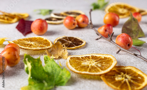 Dried sliced lemons and oranges with fresh red apples and autumn leaves on white texture surface.