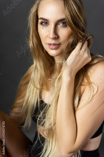 Beautiful pregnant blonde woman wearing black maternity underwear sits on a chair on a gray background and touches her hair. Health, fashion, motherhood. Close up portrait.