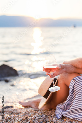 Canvas Print Girl is sitting on sea beach with wineglass of wine at sunset in summer vacation in resort