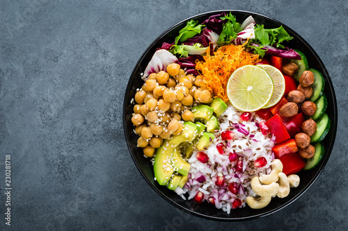 Healthy vegetarian Buddha bowl with fresh vegetable salad, rice, chickpea, avocado, sweet pepper, cucumber, carrot, pomegranate and nuts closeup