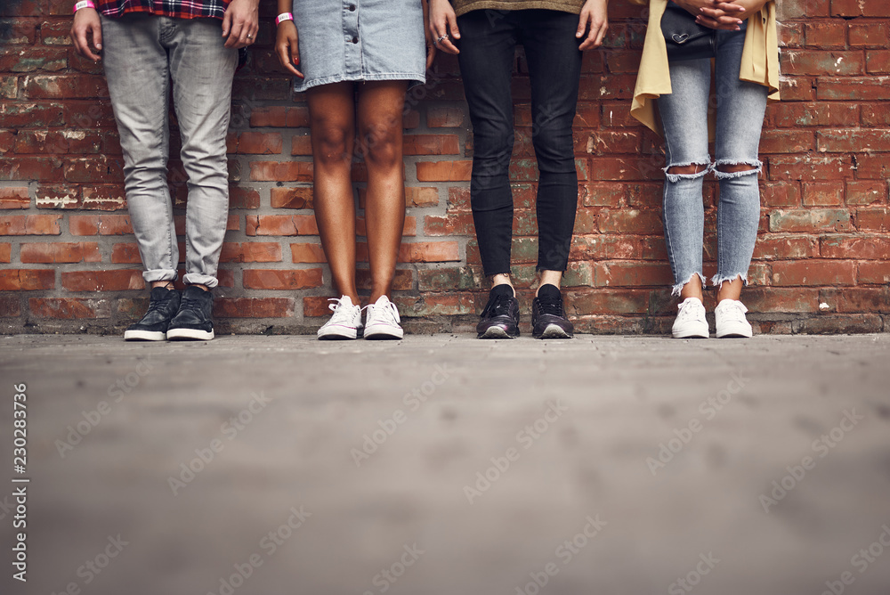 Legs of friends. Horizontal image of four stylish people standing next to the brick wall and posing for the photo Legs of friends. Horizontal image of four stylish people standing next to the brick wall and posing for the photo
