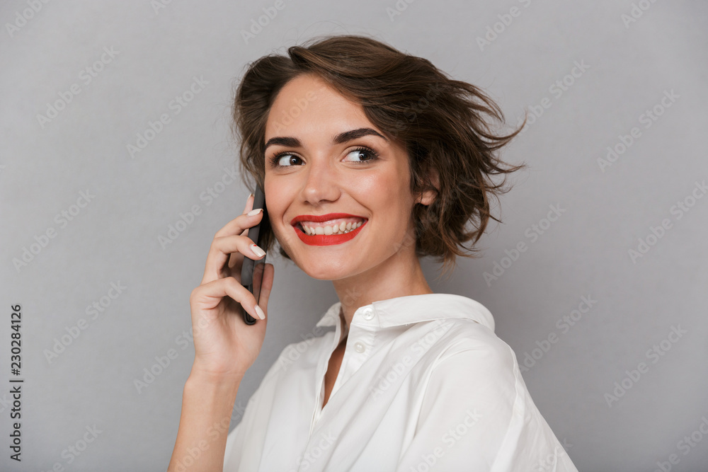 Photo of cute woman 20s smiling and speaking on mobile phone, isolated over gray background Photo of cute woman 20s smiling and speaking on mobile phone, isolated over gray background