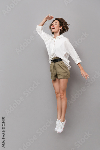 Full length image of caucasian woman 20s smiling and jumping, isolated over gray background