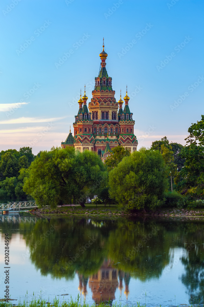 Orthodox church on the bank of Olgin pond at dusk in low light surrounded by green summer trees of the garden for walking. Peter and Paul Cathedral in Petergof, Saint Petersburg, Russia.
