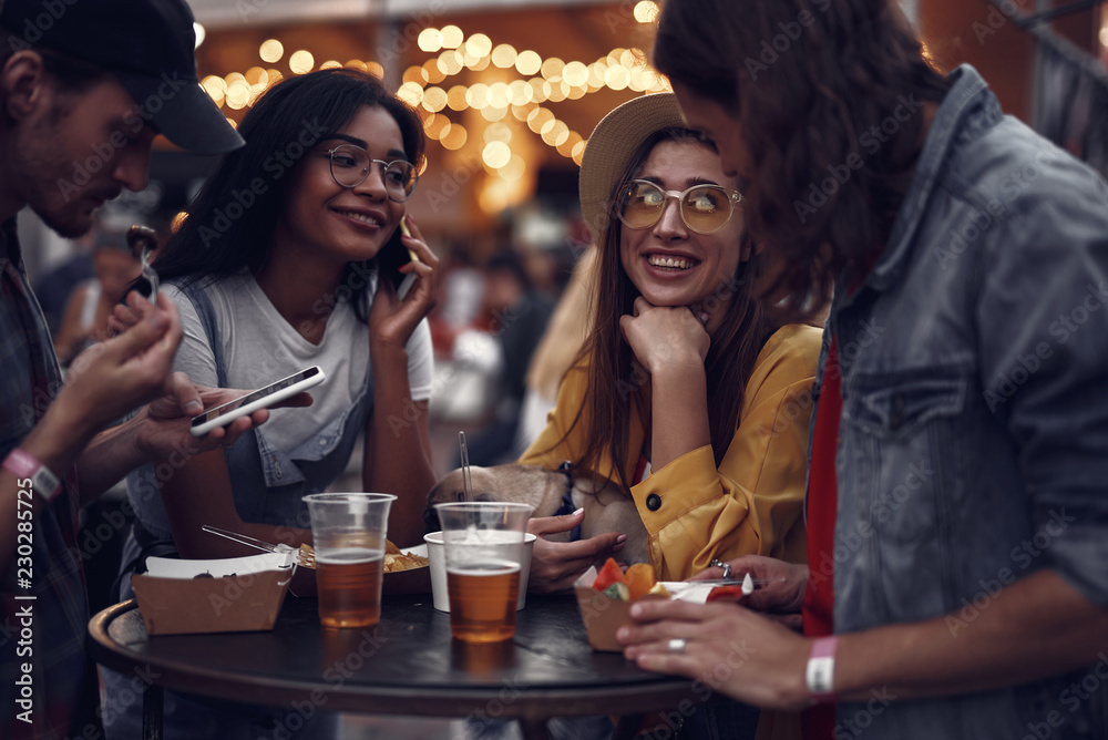 Portrait of young people standing at the table, chatting and using smartphones. Smiling girl in hat holding cute pug dog Portrait of young people standing at the table, chatting and using smartphones. Smiling girl in hat holding cute pug dog