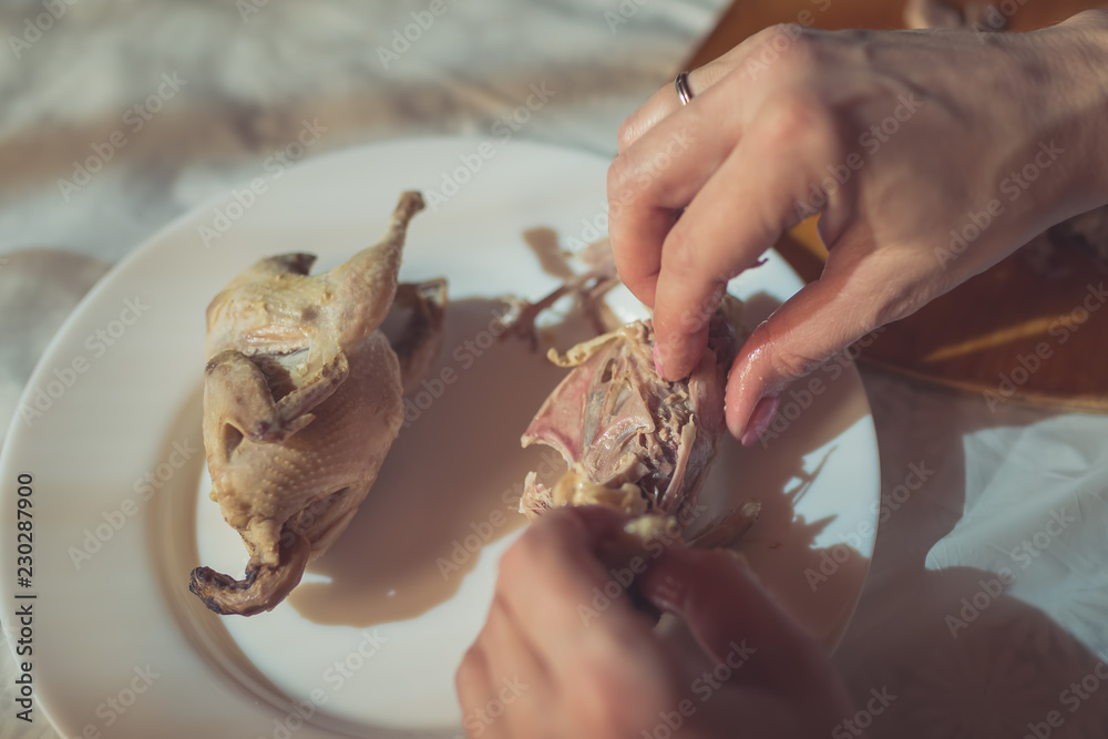 Woman is eating a cooked quail at the kitchen