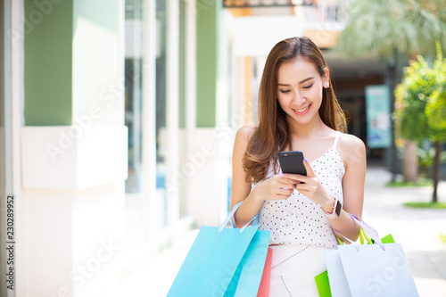 Asia woman holding many shopping bags and using smart phone at shopping mall
