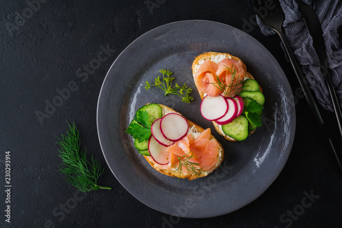 Sandwiches with smoked pink salmon, radish, cucumber and cream cheese on gray ceramic plate and textile background. Traditional Scandinavian toast. Top view.