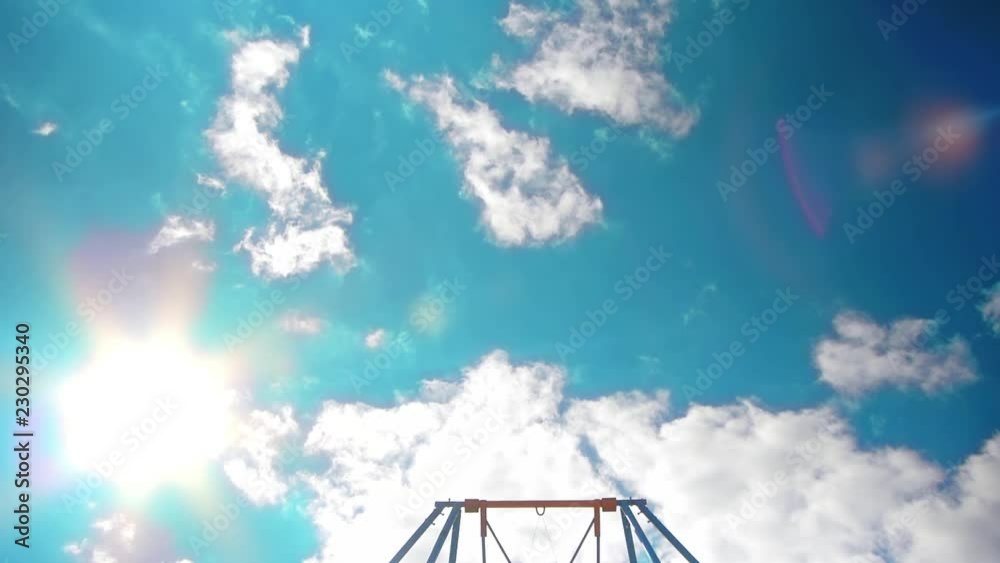 The child takes off to the sky while standing on a swing, view from below against a background of celestial blue The child takes off to the sky while standing on a swing, view from below against a background of celestial blue