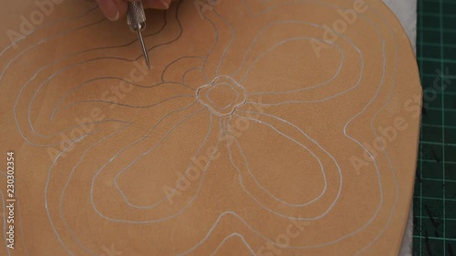 craftsman prepares the pattern on  leather for carving by awl photo