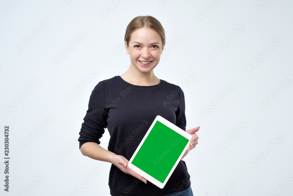 Obraz premium Caucasian woman in black clothes using digital tablet showing green screen isolated on white background. Put your advertisment here