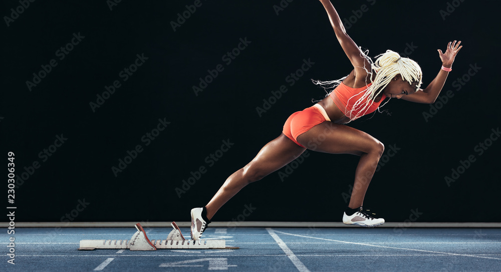 Φωτογραφία Female sprinter taking off from starting block on a running trac