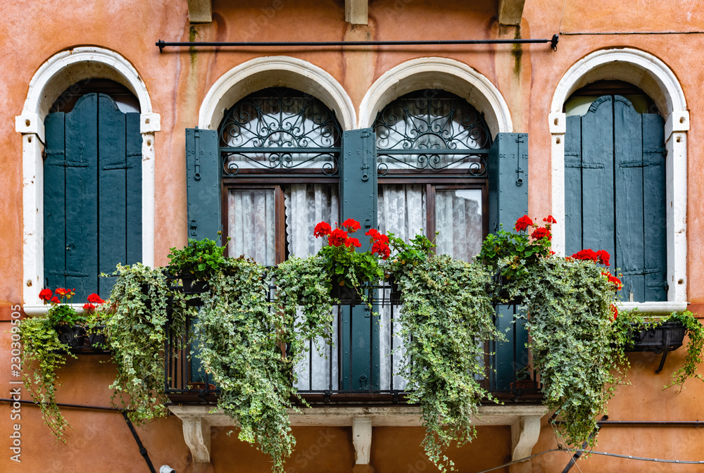 tall windows on an old balcony with flowers in italy