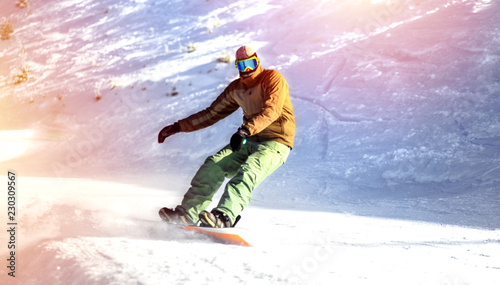 Snowboarder on snowboard piste running downhill in beautiful Alpine landscape rides through snow, explosion . Freeride snowboarding in Ski Resort . Blue sky on background. Free space for text