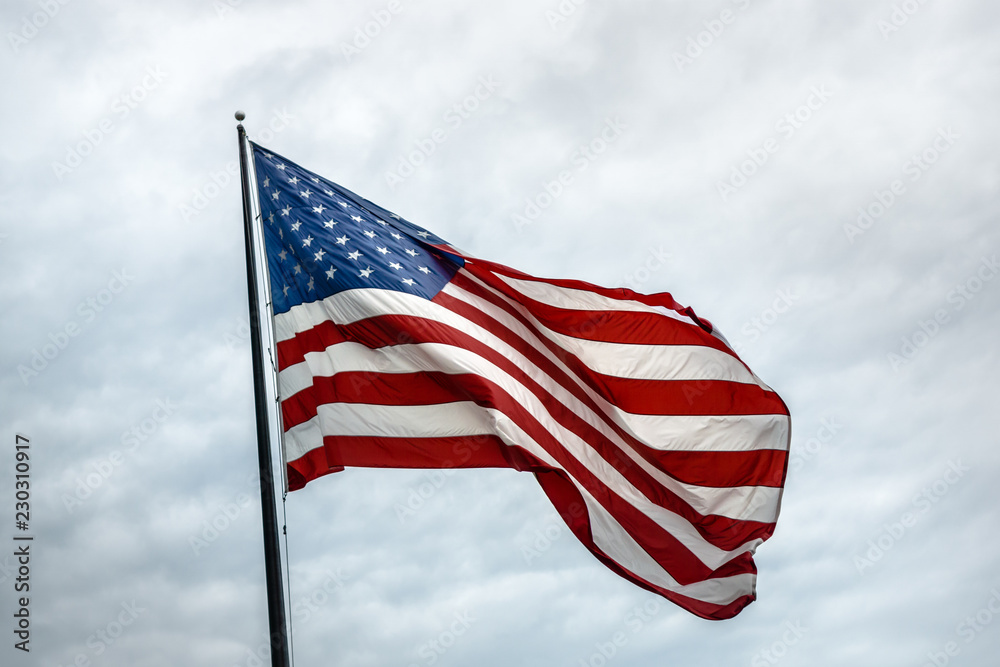A large American flag flies against a cloudy white sky