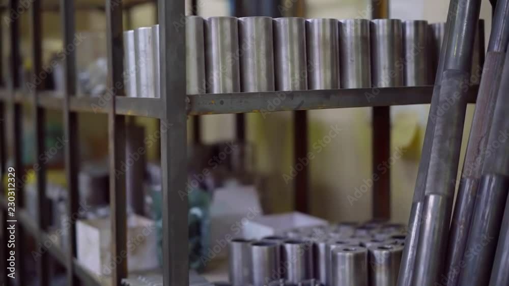 metal cylindrical billets in a metalworking shops of plant, details are standing on rack near long tubes metal cylindrical billets in a metalworking shops of plant, details are standing on rack near long tubes