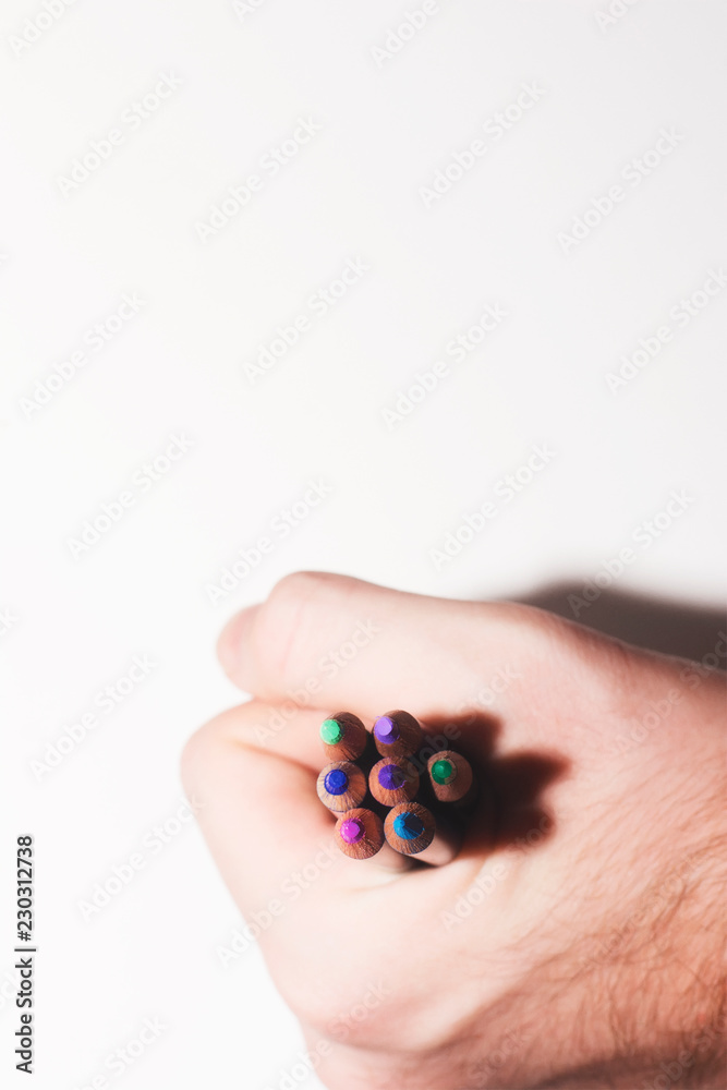 A hand holding an arrangement of cool colored pencils on an isolated paper white background