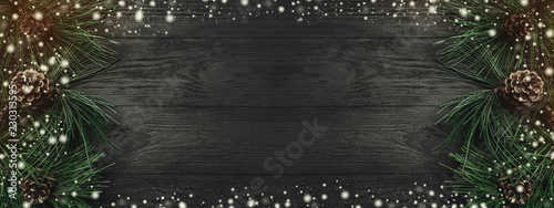 Wallpaper Mural Christmas card. Black wood background, with pine branches and pine cones from one side, top view. Xmas rectangle congratulation. Effect of light and snow. Torontodigital.ca