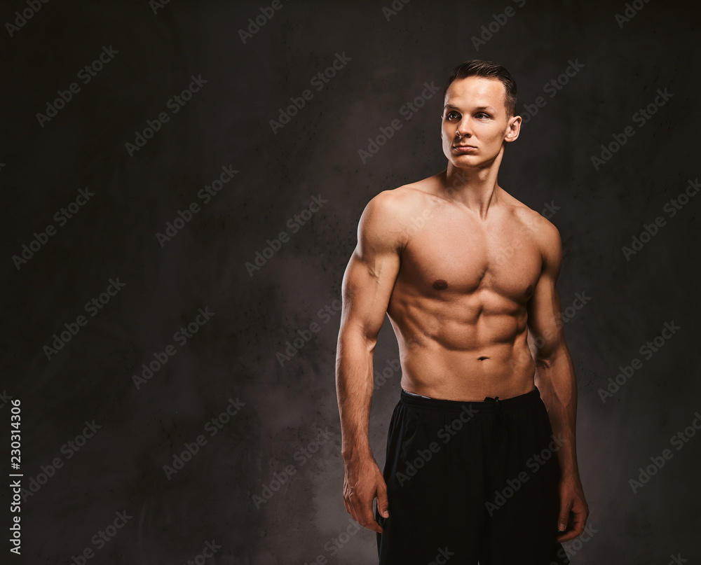 Fototapeta premium A handsome young fitness model with muscular body posing in studio on dark background.