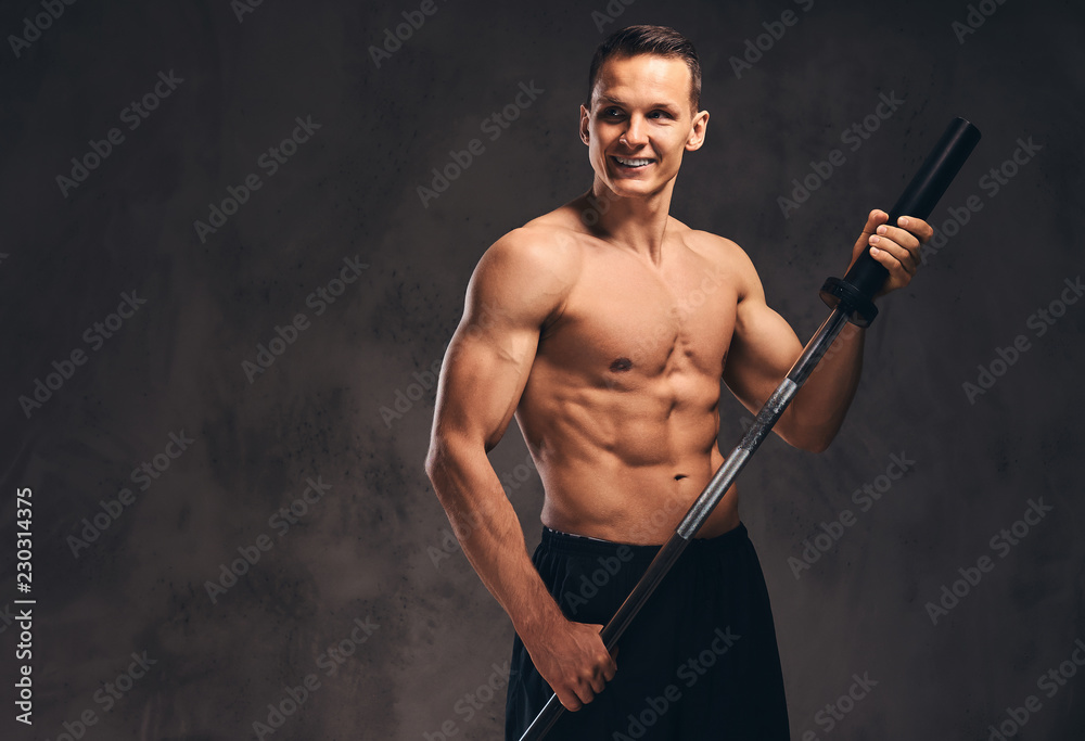 Portrait of a handsome young bodybuilder holding a barbell and looking away on dark background.