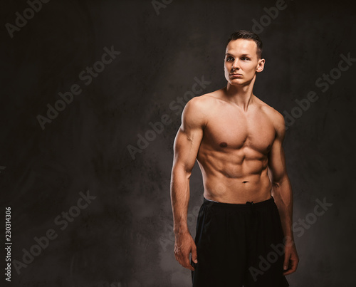 A handsome young fitness model with muscular body posing in studio on dark background. © Fxquadro