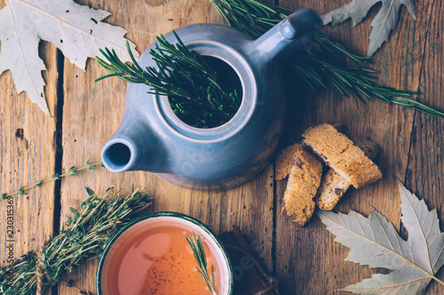 Rosemary and thyme herbal fall tea. Old wooden background with teapot, cup, herbs and leaves. Relax and peaceful mood.