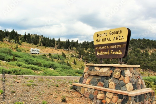 Mount Goliath Natural Area entrance in the Araphao and Roosevelt National Forest.  Mount Evans in the Colorado Rocky Mountains.  Sign and road in the foreground, hills and trees in the background 